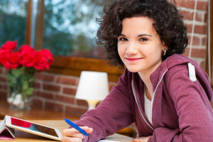 Cute Student Sitting At Table With Homework.